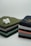 Two neatly stacked piles of folded fabrics in various colors sit on a clean surface. A cotton flower is placed on one pile, with its white fibers contrasting against the green fabric beneath it.