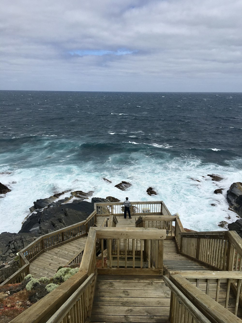 a wooden staircase leading to the ocean with a person standing on top of it