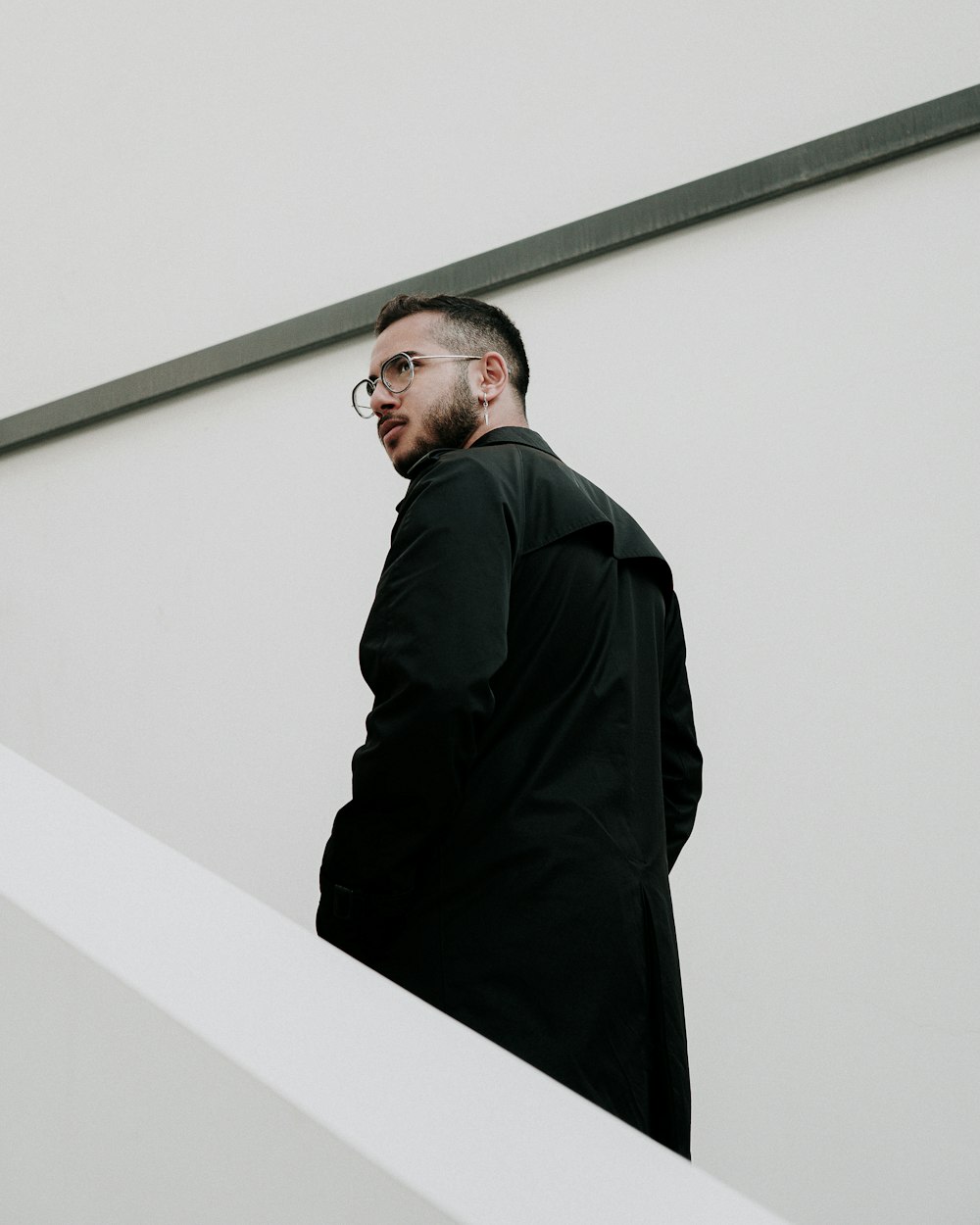 a man in a black coat and glasses standing on a staircase