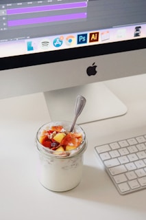 a cup of yogurt with a spoon sitting in front of a computer