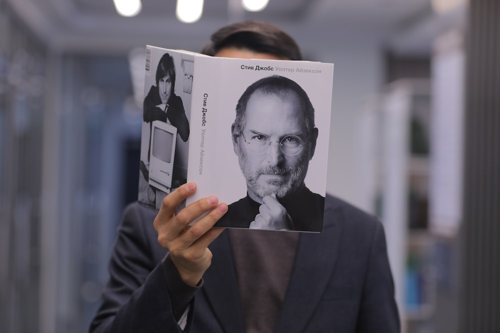 a man holding up a book with a picture of steve jobs on it