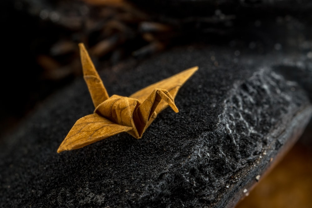 a yellow origami bird sitting on top of a black rock