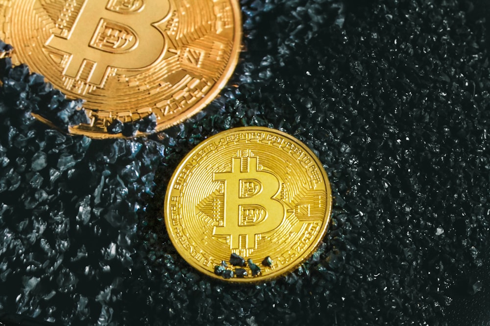 two gold bitcoins sitting on a black surface