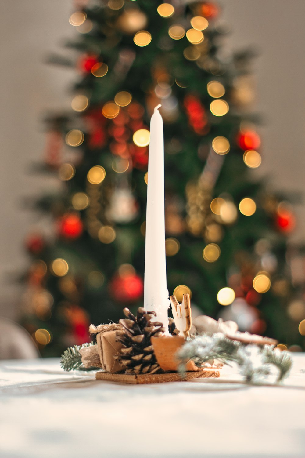 a white candle sitting on top of a table next to a christmas tree