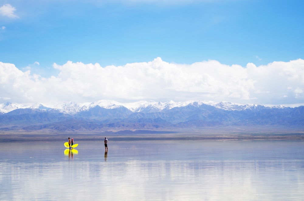 two people standing in the water with a surfboard