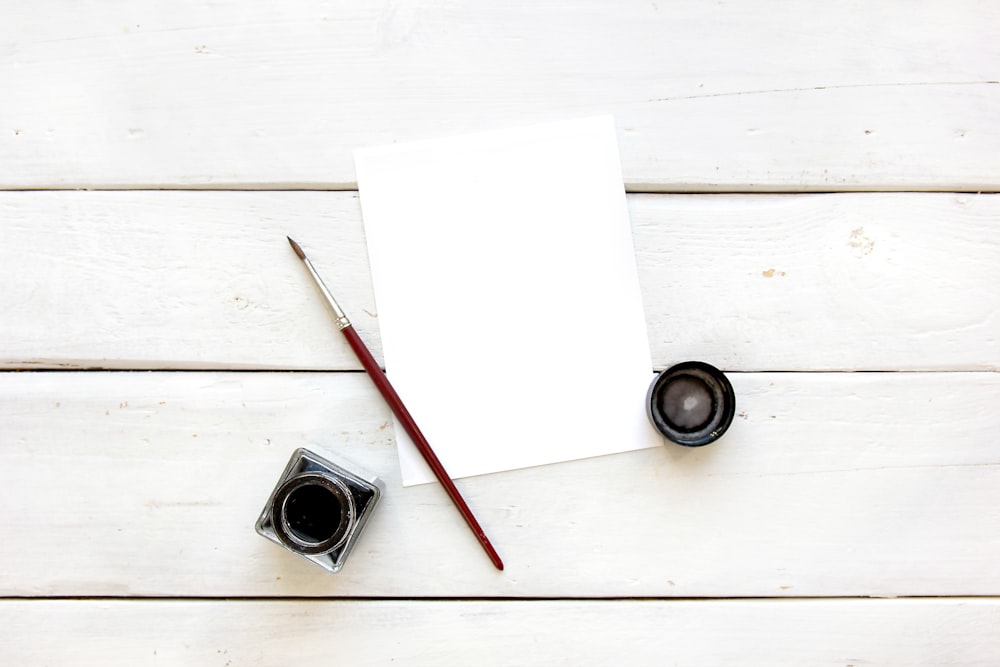a blank sheet of paper next to a cup of ink and a brush