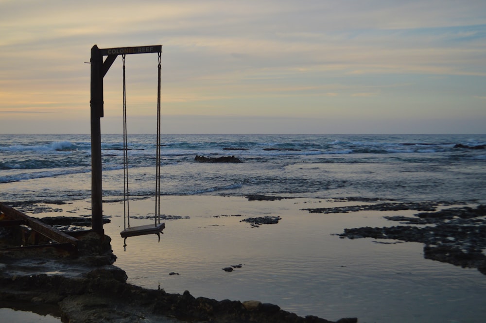 a swing sitting on top of a beach next to the ocean