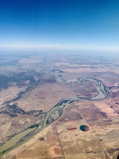 Aerial view of vast Brazilian farmland with green fields and a winding river under a clear sky.