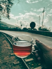 a person holding a glass of tea on a train track
