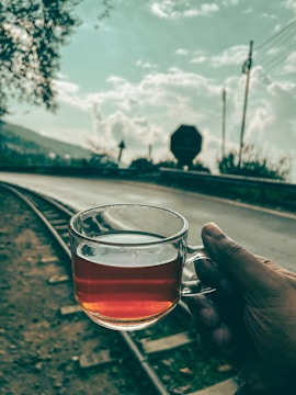 a person holding a glass of tea on a train track