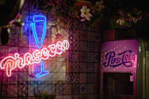 a pink pepsi cola machine sitting next to a neon sign