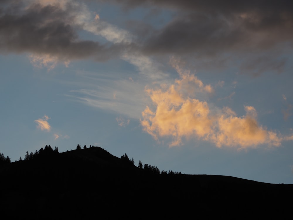 uma silhueta de uma colina com árvores e nuvens no fundo