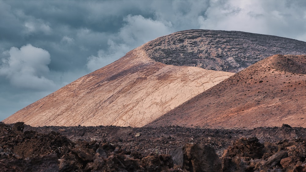 a mountain covered in dirt under a cloudy sky