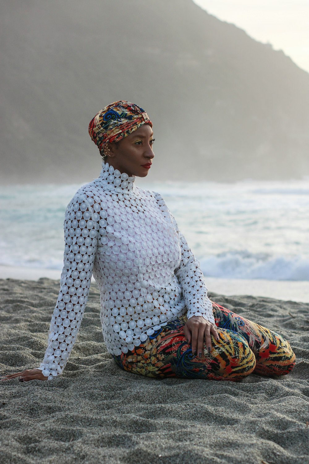 a woman sitting on the beach in a white top