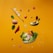 A vibrant display of floating food items includes an avocado half, a brown egg, cherry tomatoes, a slice of red bell pepper, almonds, and leafy greens. Among them, a fork and letter tiles spelling 'KETO' are interspersed. The background features a warm, mustard yellow color.