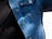 A close-up view of a person wearing a denim jacket with metal buttons and a black shirt underneath. The denim fabric shows various shades of blue, with visible stitching and a pocket on the chest. There are shadows cast on the jacket, indicating natural light.