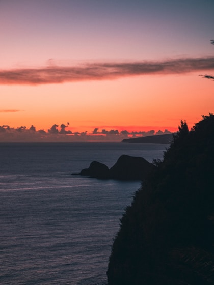 the sun is setting over the ocean with rocks in the foreground