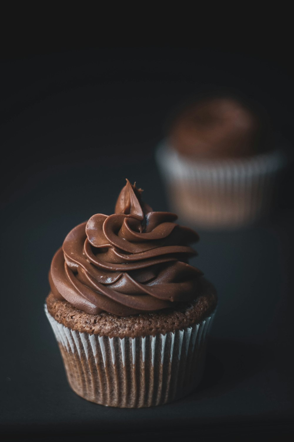 a chocolate cupcake with chocolate frosting on a black background