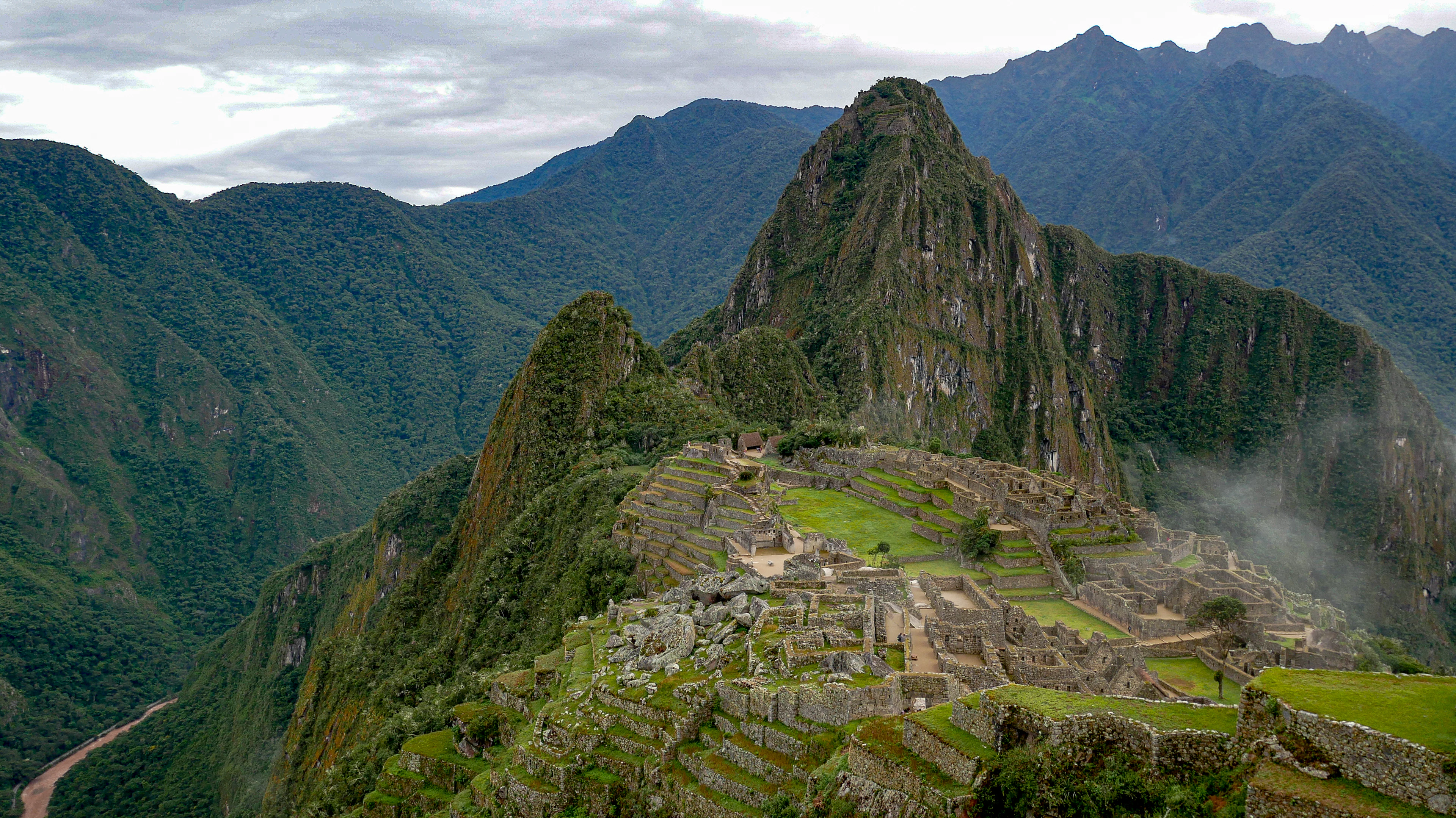 The terraces and stone buildings of Machu Picchu among green mountains, with the Urubamba River winding below, Peru