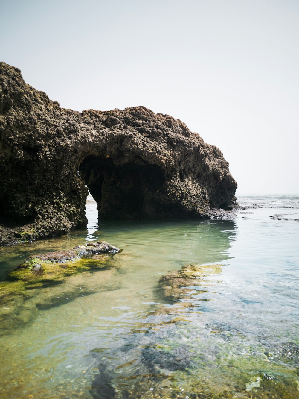 a large rock formation in the water near a beach