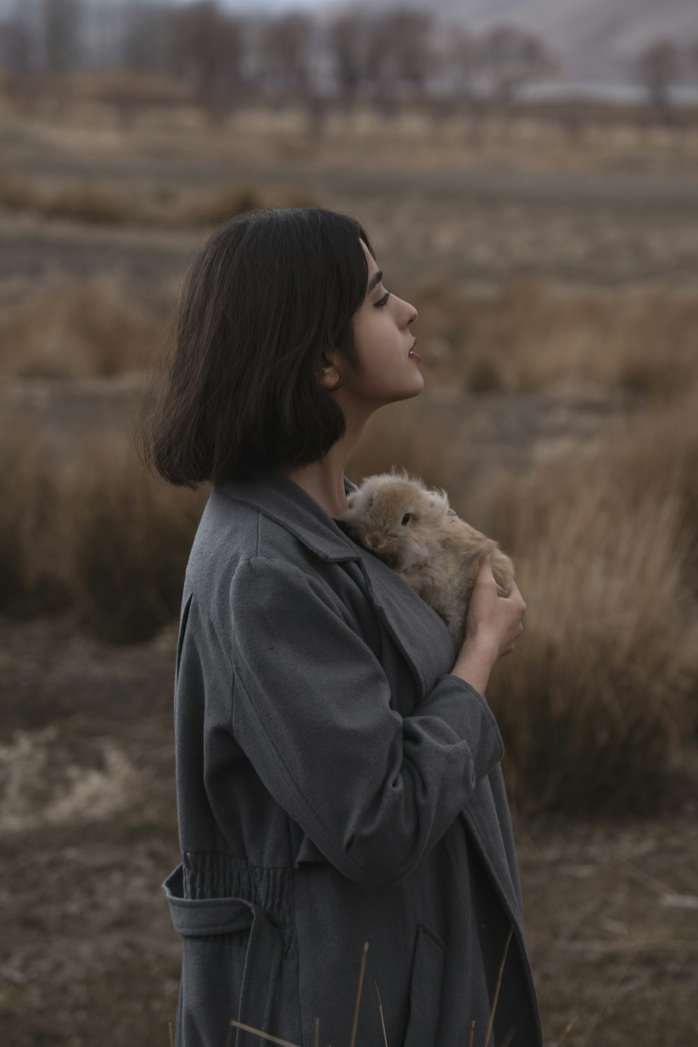 a woman standing in a field holding a teddy bear