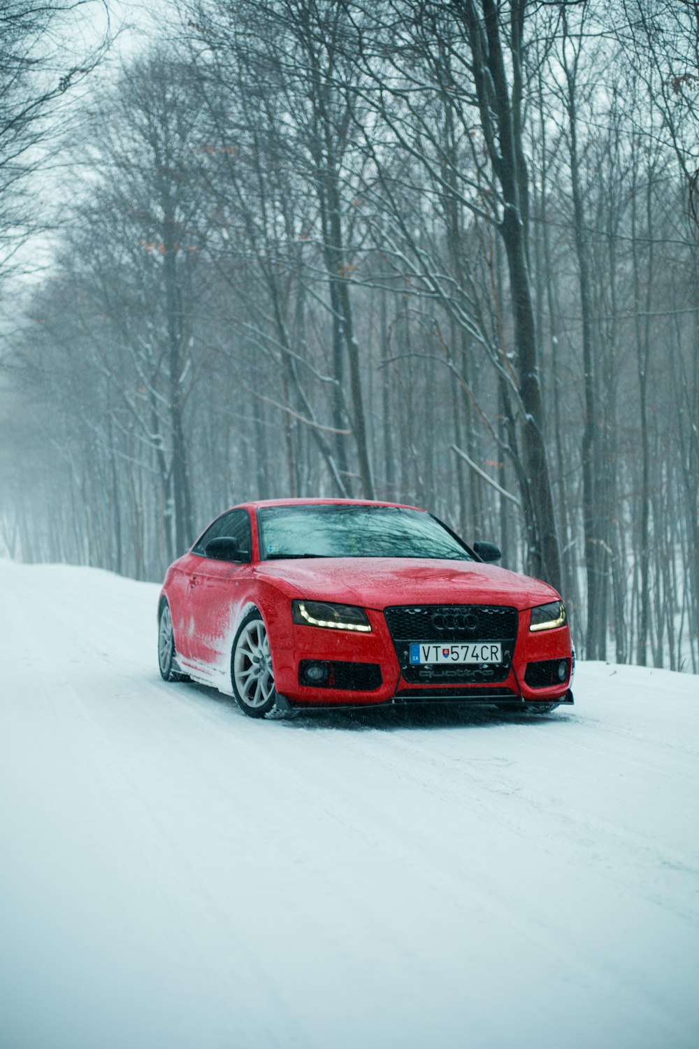 a red car driving down a snow covered road