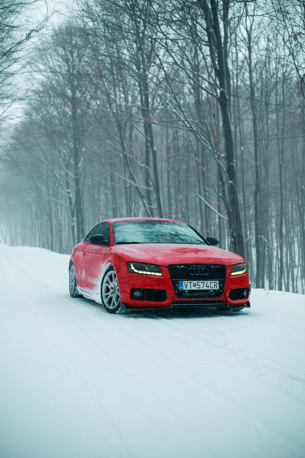 um carro vermelho dirigindo por uma estrada coberta de neve