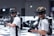 Two individuals are wearing virtual reality headsets and carrying gaming guns. Each person is equipped with a sturdy-looking backpack, possibly housing electronics needed for the VR experience. They are standing in an indoor environment, likely a virtual reality gaming arena, which has a modern and high-tech appearance. The background is slightly blurred, emphasizing the focus on the individuals.