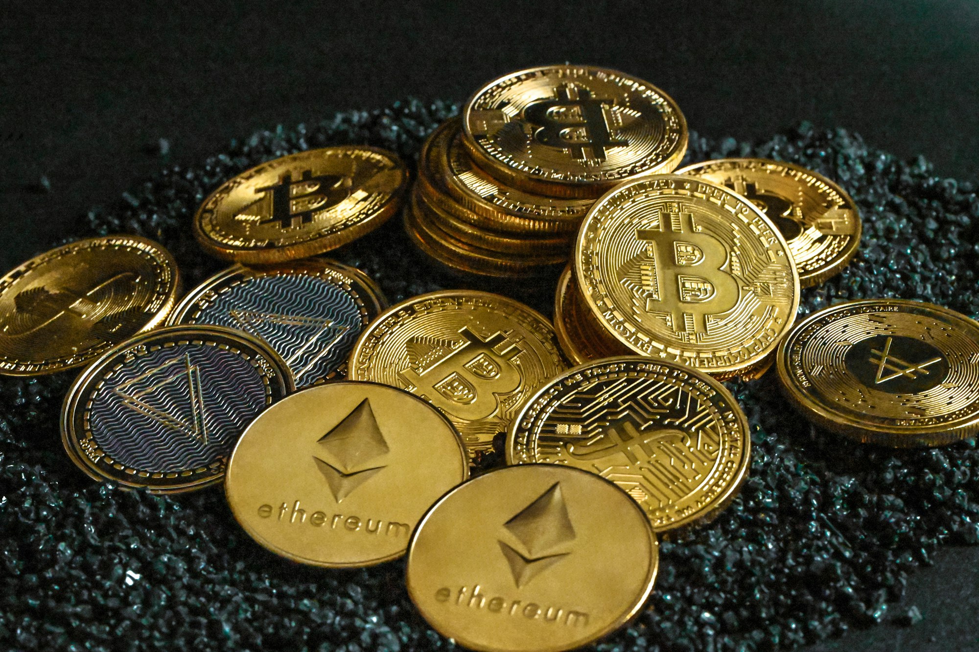 A group of gold cryptocurrency coins on top of black stones

