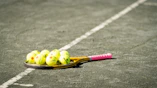 a tennis racket and four tennis balls on a tennis court
