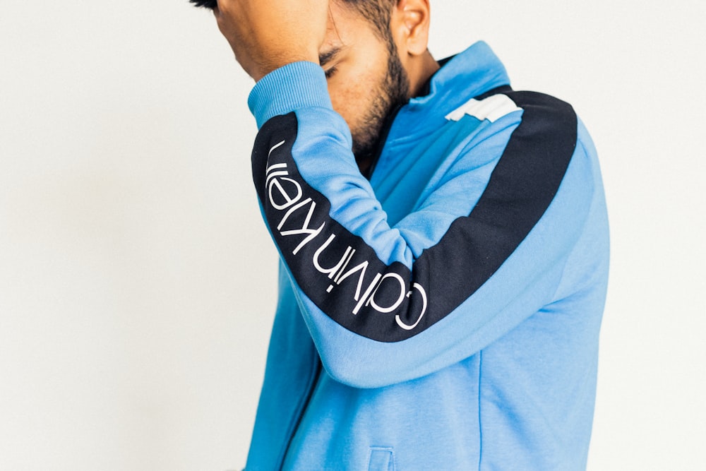 a man in a blue hoodie covers his face with his hands