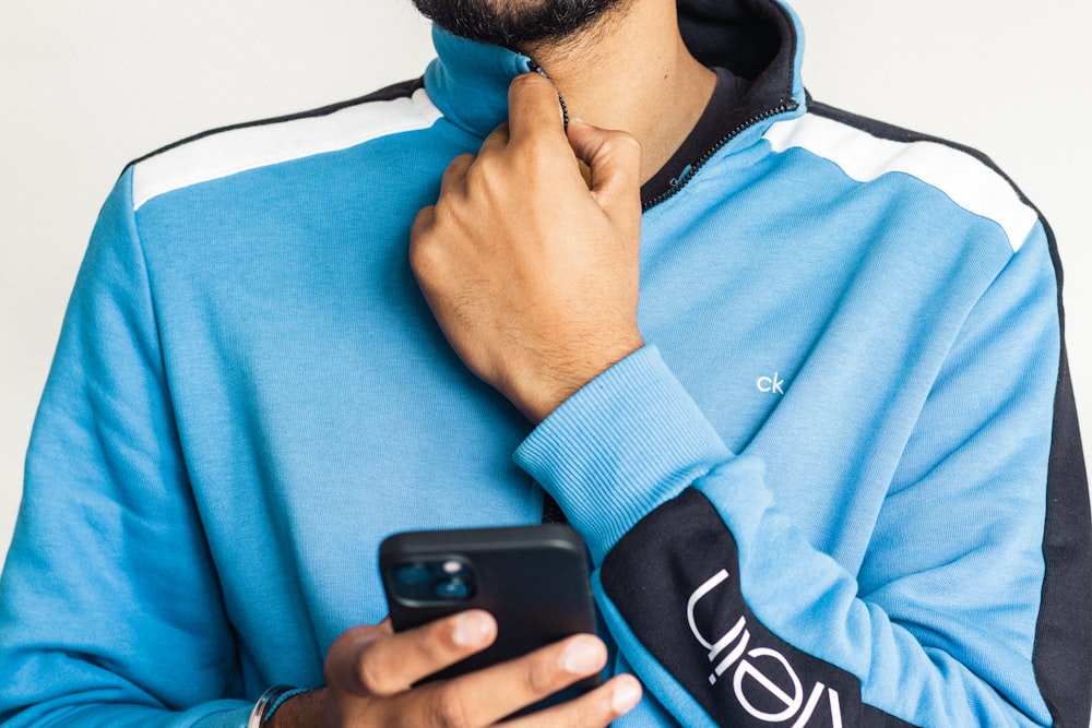 Un uomo con una felpa blu con cappuccio che tiene un telefono cellulare