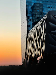 A sleek 3D architectural rendering of a modern glass building at sunset.