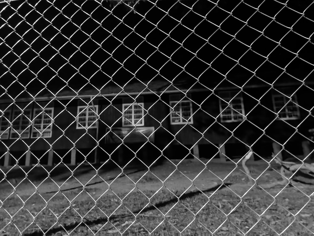 a black and white photo of a house through a chain link fence