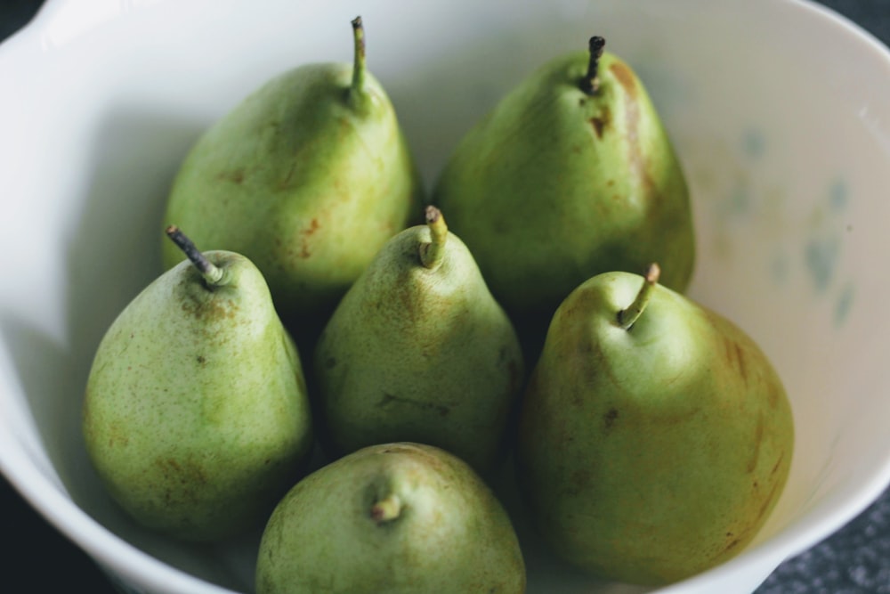 a white bowl filled with green pears on top of a table