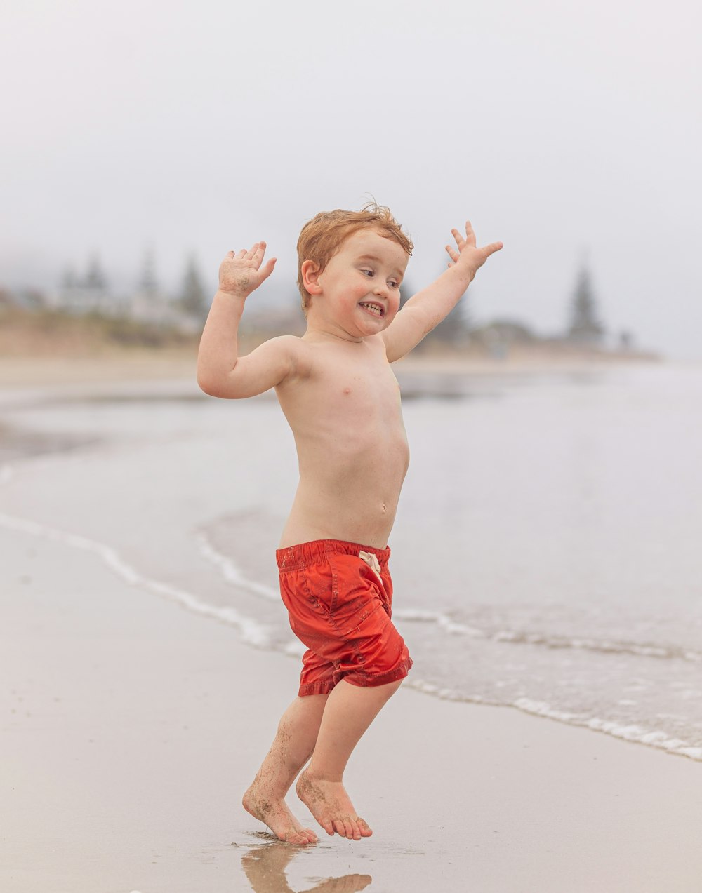 a little boy running on the beach with his hands in the air