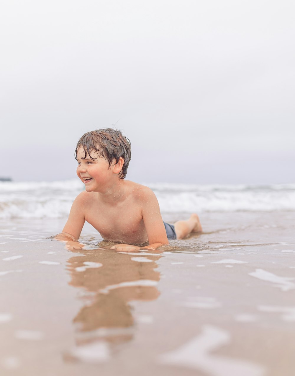 a young boy laying on his stomach in the ocean