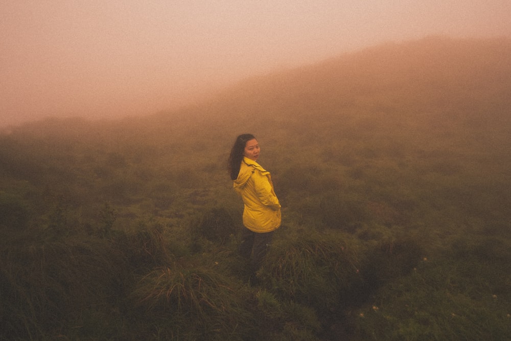 a woman in a yellow jacket standing in a foggy field