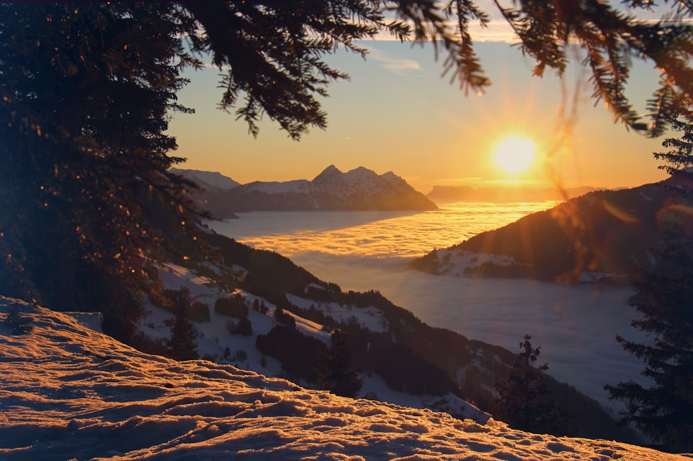 the sun is setting over a snowy mountain range