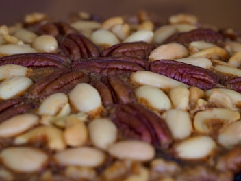 A close-up view of a baked treat featuring a dense layer of mixed nuts, including pecans and almonds, arranged decoratively on top.