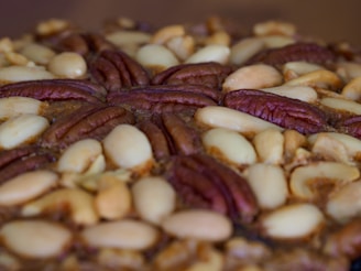 A close-up view of a baked treat featuring a dense layer of mixed nuts, including pecans and almonds, arranged decoratively on top.