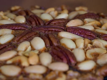 A close-up view of a baked treat featuring a dense layer of mixed nuts, including pecans and almonds, arranged decoratively on top.