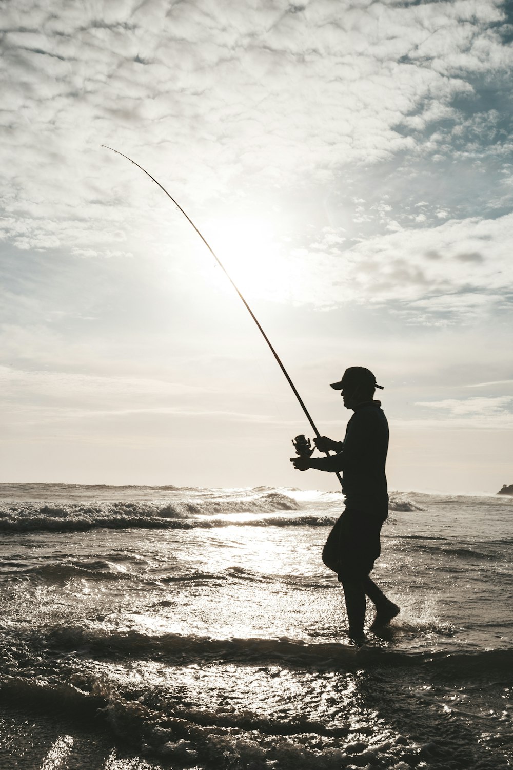 um homem de pé no oceano enquanto segura uma vara de pesca