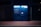 A blue Amazon parcel locker is illuminated against a dark background, featuring compartments and a screen for package retrieval. It displays phrases in Italian, suggesting its use for ordering and pickup.
