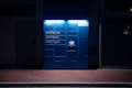 A blue Amazon parcel locker is illuminated against a dark background, featuring compartments and a screen for package retrieval. It displays phrases in Italian, suggesting its use for ordering and pickup.