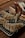 A hand is piping white icing in a zigzag pattern onto freshly baked puff pastries. The pastries are placed on a metal cooling rack over a wooden table. The pastries are golden brown with a flaky texture, and the icing adds a decorative finishing touch.