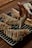 A hand is piping white icing in a zigzag pattern onto freshly baked puff pastries. The pastries are placed on a metal cooling rack over a wooden table. The pastries are golden brown with a flaky texture, and the icing adds a decorative finishing touch.