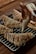 A hand is piping white icing in a zigzag pattern onto freshly baked puff pastries. The pastries are placed on a metal cooling rack over a wooden table. The pastries are golden brown with a flaky texture, and the icing adds a decorative finishing touch.