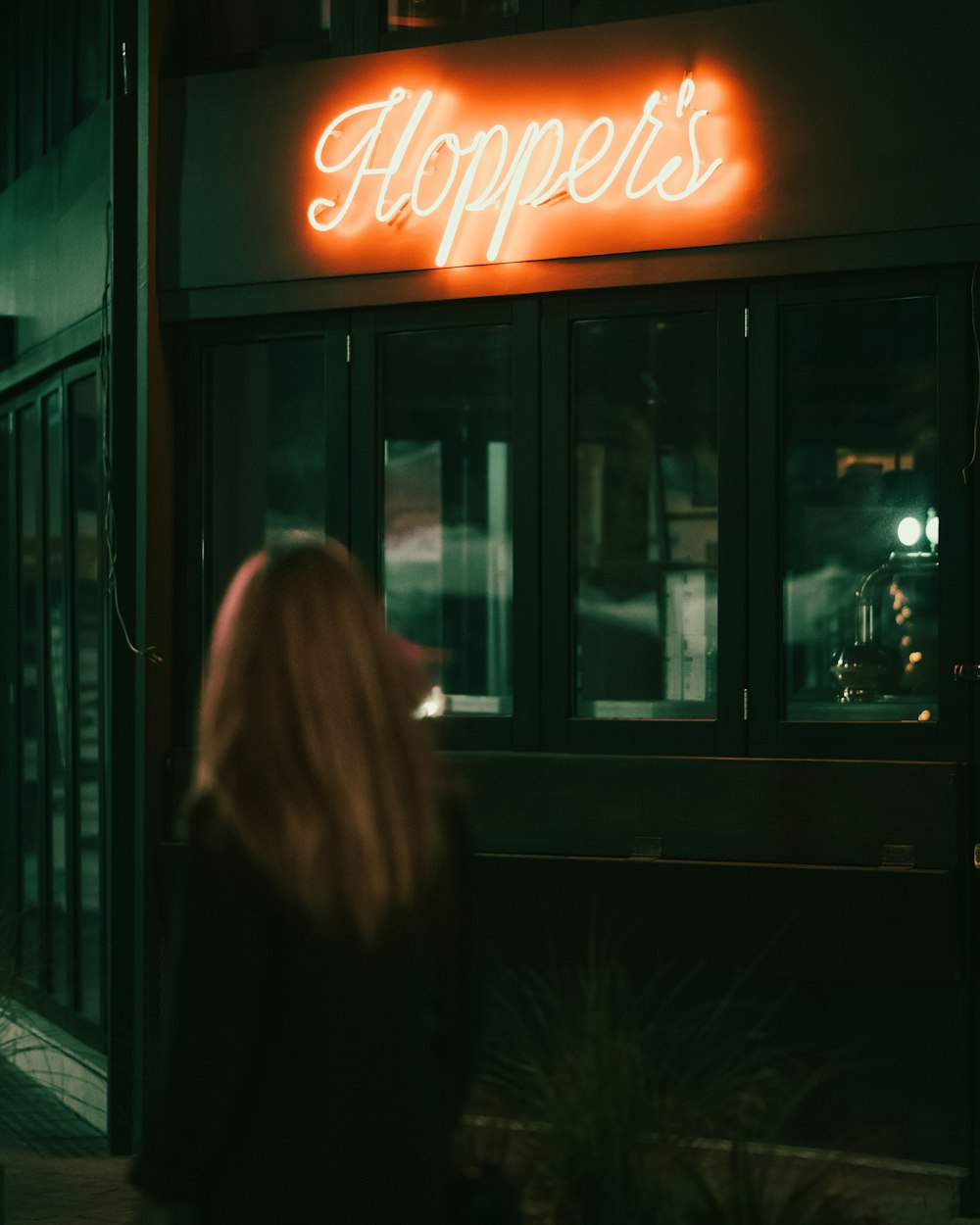 a woman standing outside of a restaurant at night