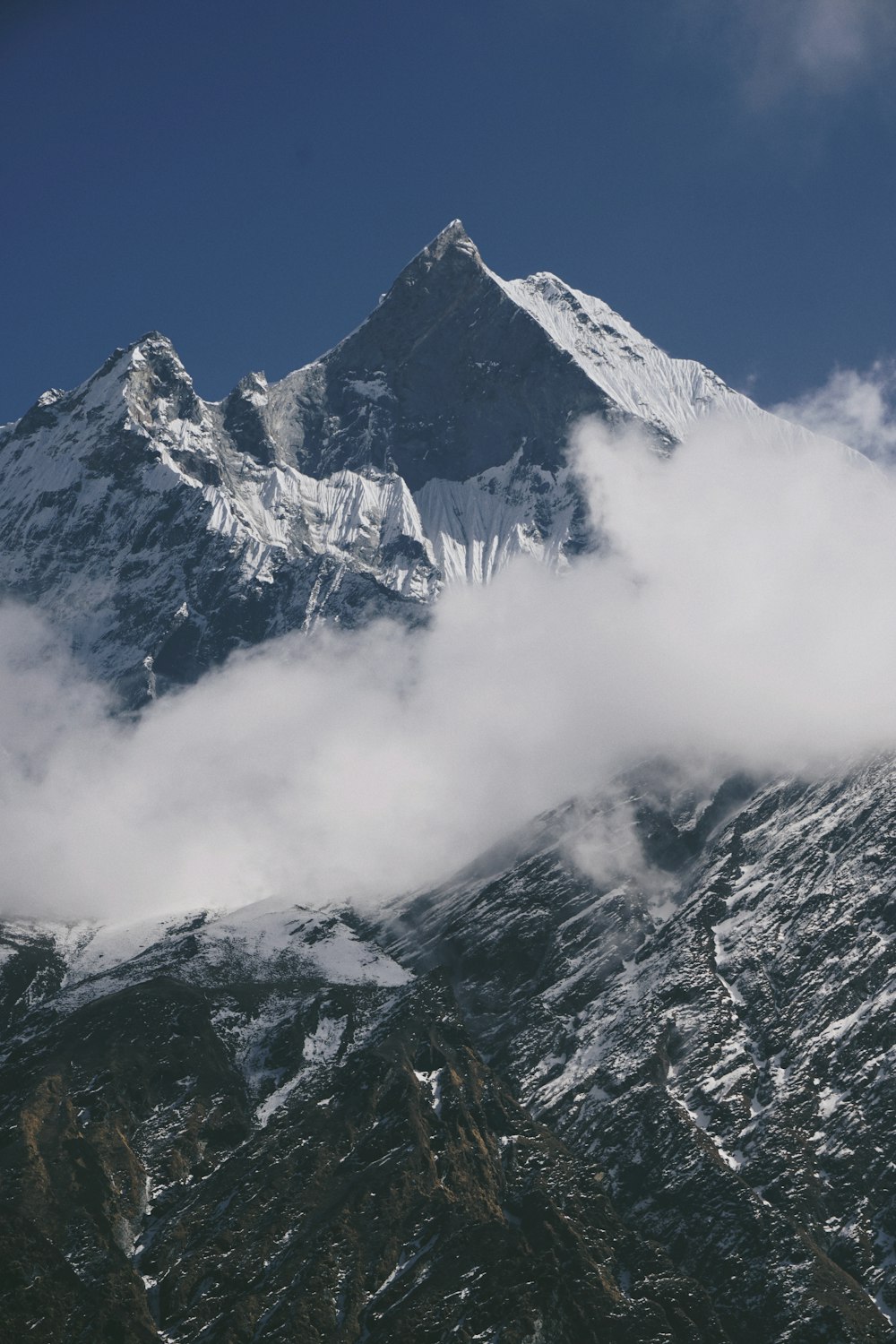 a mountain covered in snow and clouds under a blue sky